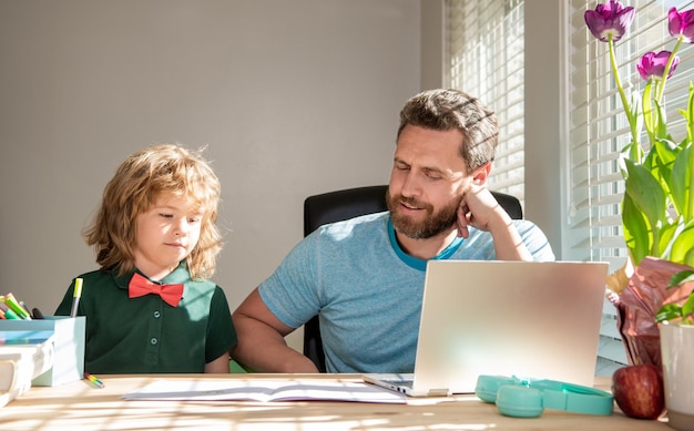 Insegnante uomo maturo o papà che aiuta il figlio del bambino con i compiti a scuola sul computer per tornare a scuola