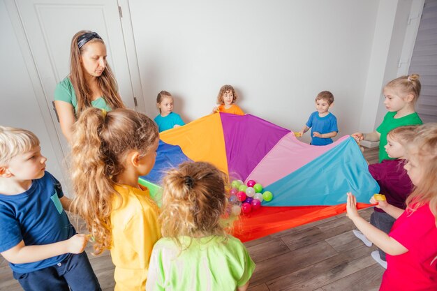 Insegnanti e bambini della scuola materna che giocano con il paracadute colorato