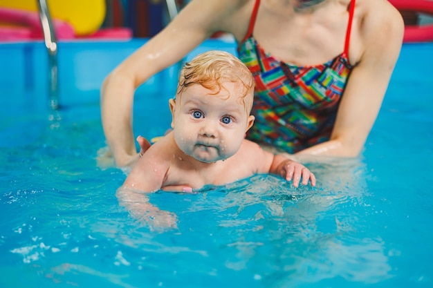 Insegnare a un neonato a nuotare in piscina con un allenatore Corsi di nuoto per bambini Il bambino nuota in piscina