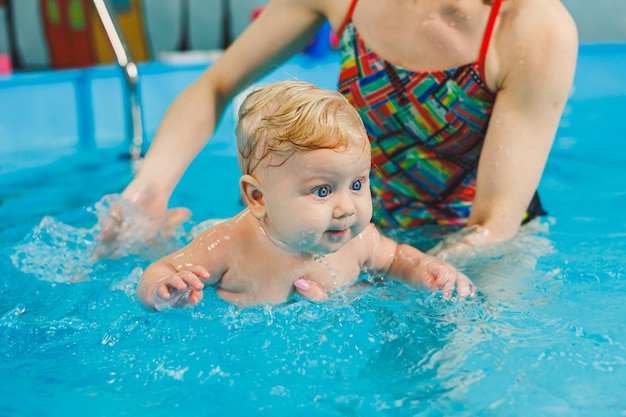 Insegnare a un neonato a nuotare in piscina con un allenatore Corsi di nuoto per neonati Il bambino nuota in piscina