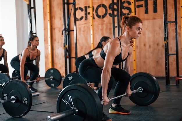 Insieme ai bilancieri Un gruppo di giovani sportivi ha una giornata di crossfit al chiuso in palestra