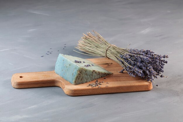 Insolito formaggio blu con sapore di lavanda sul tagliere di legno accanto al bouquet di lavanda profumata.