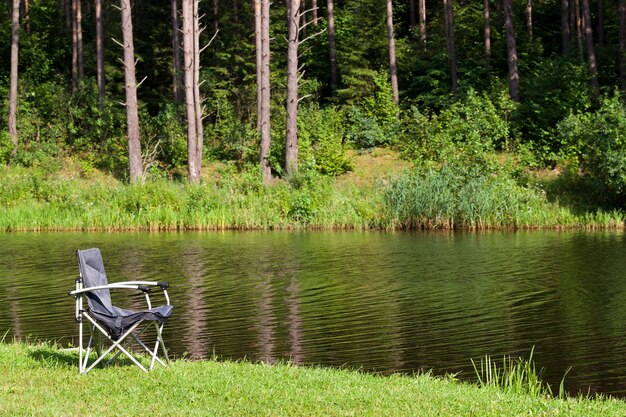 Installato sulla riva del fiume nella foresta sedia pieghevole in metallo per la pesca, estate