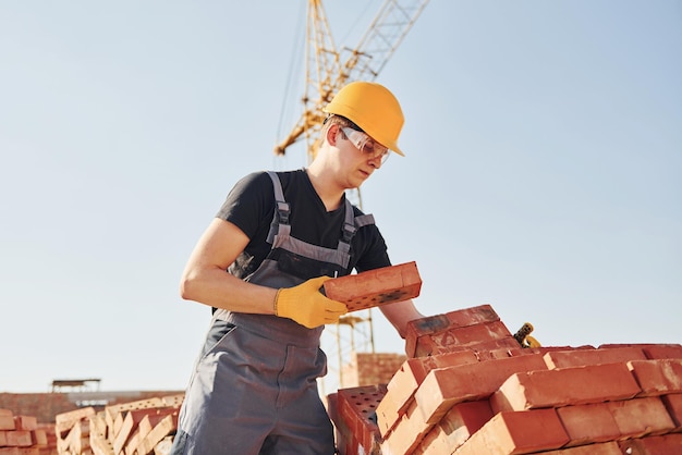 Installazione del muro di mattoni Il lavoratore edile in uniforme e le attrezzature di sicurezza hanno un lavoro sulla costruzione