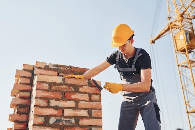 Installazione del muro di mattoni Il lavoratore edile in uniforme e le attrezzature di sicurezza hanno un lavoro sulla costruzione