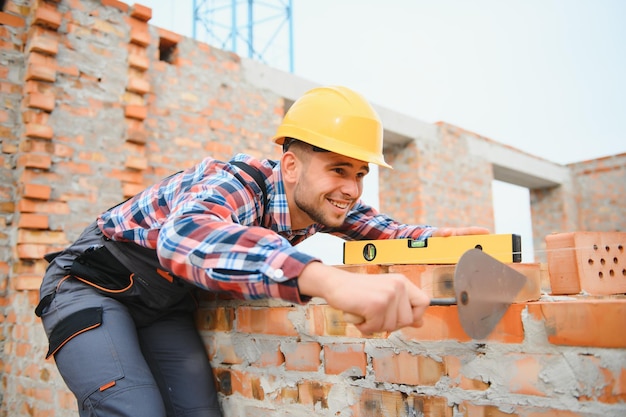 Installazione del muro di mattoni Il lavoratore edile in uniforme e le attrezzature di sicurezza hanno un lavoro sulla costruzione