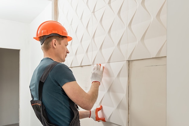 Installazione di pannelli 3D in gesso. Il lavoratore sta attaccando la piastrella di gesso al muro.