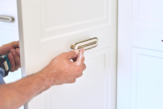 Installazione di un nuovo armadio, primo piano delle mani dell'artigiano falegname che lavora con lo strumento, set di maniglie delle porte