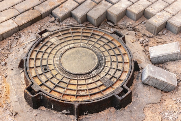 Installazione di un tombino fognario in ghisa pesante su un pozzo prima delle lastre di pavimentazione. Sistema fognario in costruzione. Avvicinamento.