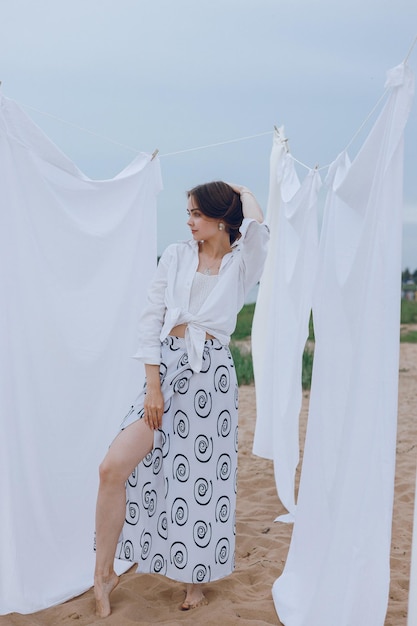 Integrale del modello femminile sottile ed elegante in lino bianco in piedi vicino alla lavanderia asciutta all'aperto