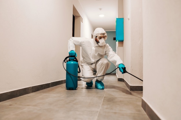 Integrale dell'uomo in vestito sterile che disinfetta la sala dell'edificio. Protezione dal concetto corona.