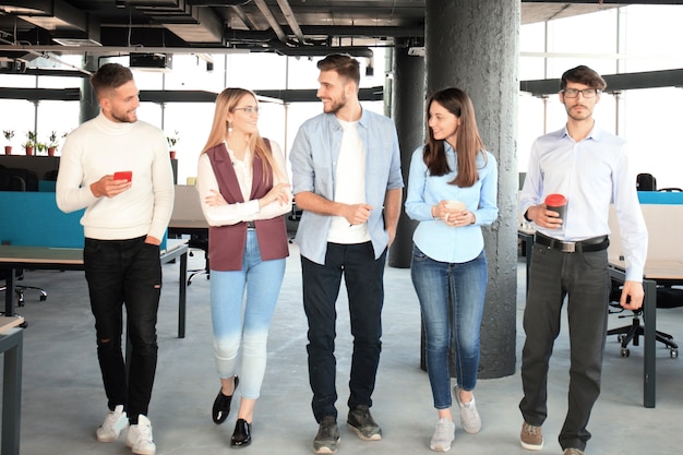 Integrale di giovani in abbigliamento casual intelligente che discutono di affari e sorridono mentre camminano per l'ufficio.