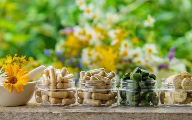 integratori e vitamine in barattoli di vetro su un tavolo di legno con sfondo di fiori sfocati