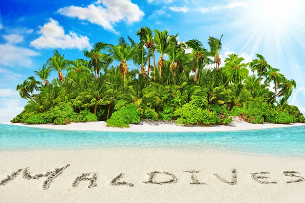 Intera isola tropicale all'interno di un atollo nell'Oceano tropicale. Isola subtropicale disabitata e selvaggia con palme. Iscrizione "Maldive" nella sabbia su un'isola tropicale, Maldive.