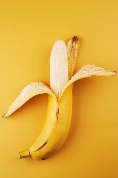 Intera mezza banana sbucciata isolata su fondo giallo da vicino