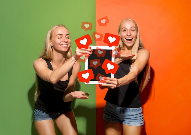 Interazioni sui social media sul cellulare. Marketing digitale su Internet, chat, commenti, mi piace. Sorrisi e icone sopra lo schermo dello smartphone, che tengono in mano le giovani donne sullo sfondo luminoso dello studio.