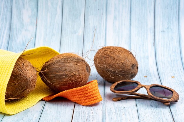 Intere noci di cocco che si trovano in un sacchetto giallo e bicchieri su uno sfondo di legno blu.