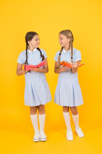 Interesse sincero. Biblioteca scolastica. Libri didattici per la scuola. Leggendo libri. Leggere e raccontare. Bambini piccoli in possesso di libri sfondo giallo. Bambine con enciclopedia o libri per bambini.