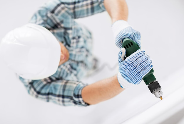 interior design e concetto di ristrutturazione della casa - uomo in casco con trapano elettrico che fa un foro nel muro