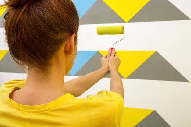 Interior design. La ragazza dipinge il muro di giallo. rullo e vassoio di vernice.
