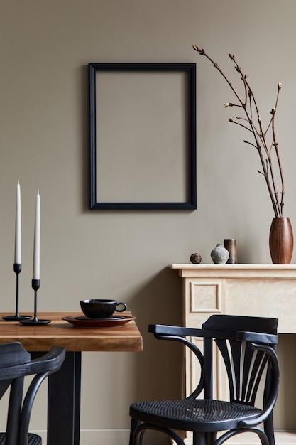 Interior design rustico della sala da pranzo con tavolo familiare in legno, candelabro, sedia retrò, tazza di caffè, decorazione, cornice ed eleganti accessori personali. Muro beige.