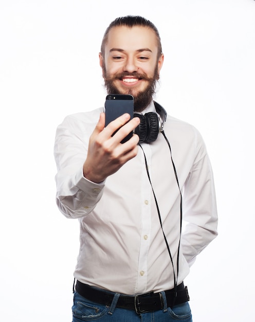 Internet, tecnologia e concetto di persone. un giovane uomo con la barba in camicia che tiene il telefono cellulare e che fa foto di se stesso mentre levandosi in piedi su bianco