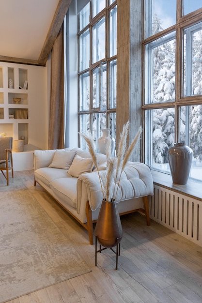 Interni accoglienti e caldi di un elegante chalet di campagna con un'enorme finestra panoramica che si affaccia sulla foresta invernale decorazioni in legno a pianta aperta colori caldi e un focolare familiare