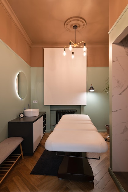 Interni classici dell'ufficio di cosmetologia con un lavandino un letto e una sedia di bellezza per il viso completamente elettrici uno sgabello da salone una lampada a led in un salone Una tenda della finestra abbassata