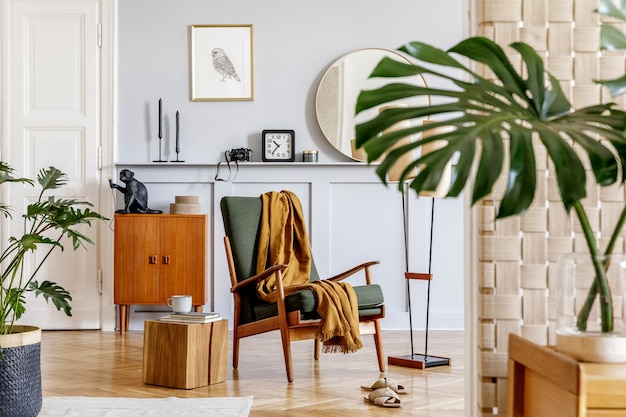 Interni eleganti del soggiorno con poltrona di design, comò vintage in legno, specchio rotondo, mensola, foglia tropicale, tavolino da caffè, decorazione, tappeto e accessori personali nell'arredamento della casa.