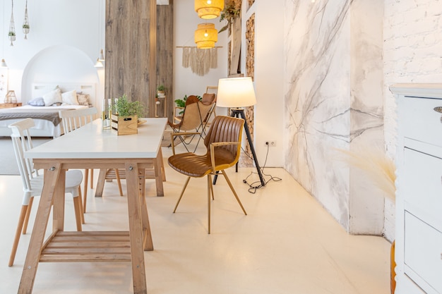 Interni moderni alla moda di un monolocale luminoso con colonne in legno in stile loft, decorato con mattoni, marmo e legno con mobili eleganti e pareti bianche