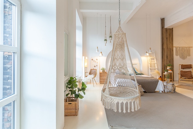 Interni moderni alla moda di un monolocale luminoso con colonne in legno in stile loft, decorato con mattoni, marmo e legno con mobili eleganti e pareti bianche