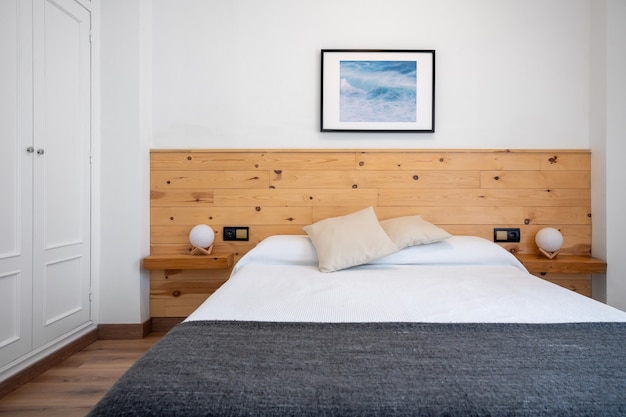 Interno bianco luminoso della camera da letto decorato con una foto delle onde del mare e una testiera in legno