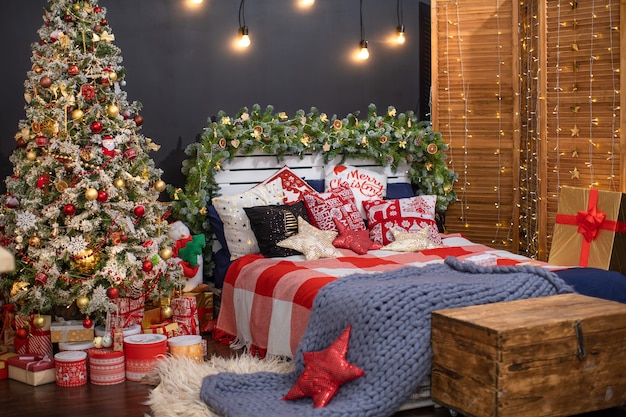 Interno camera da letto nella decorazione scura decorata per Natale. il letto con lino blu scuro e molti cuscini è ricoperto da una coperta di lana fatta di filato di pecora Hyper large