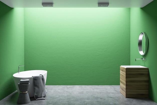 Interno del bagno minimalista con pareti verdi, pavimento di cemento, vasca bianca e lavandino di legno. Uno specchio rotondo.