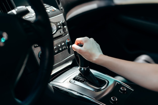 Interno del salone dell'automobile nera. Mano femminile sulla trasmissione