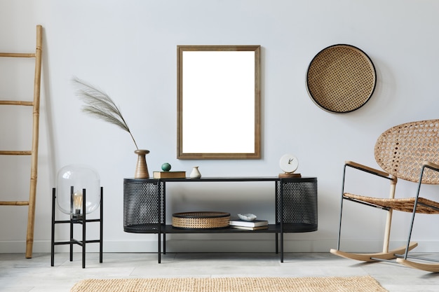 Interno moderno del soggiorno scandinavo con cornice per poster finto, comò di design, foglia in vaso, poltrona in rattan, libro e accessori eleganti in un elegante arredamento per la casa. Modello.