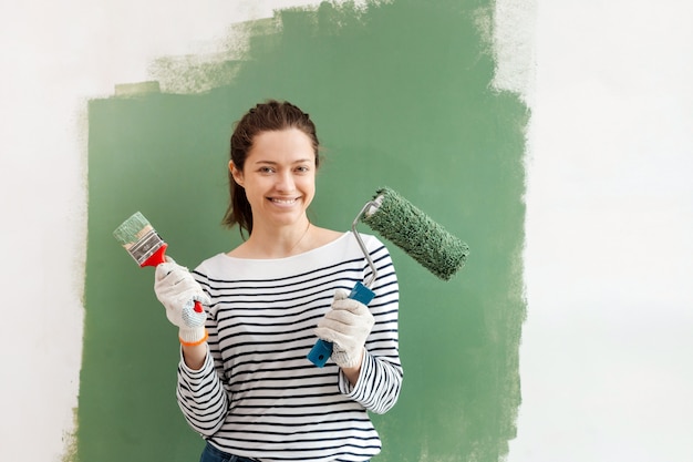 Interno paiting della parete della giovane donna con il rullo e la spazzola di pittura