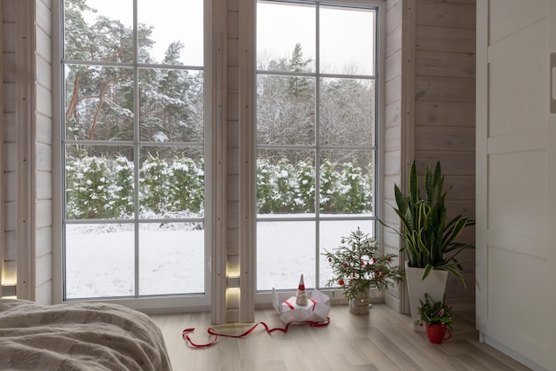 Interno scandinavo del salone in una casa di legno. Decorazione della stanza di Natale, albero di Natale e regalo, grande finestra
