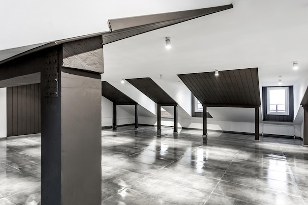 Interno vuoto della camera mansardata del loft non arredato con colonne in legno e pavimento in cemento bagnato a livello del tetto in colore nero e bianco