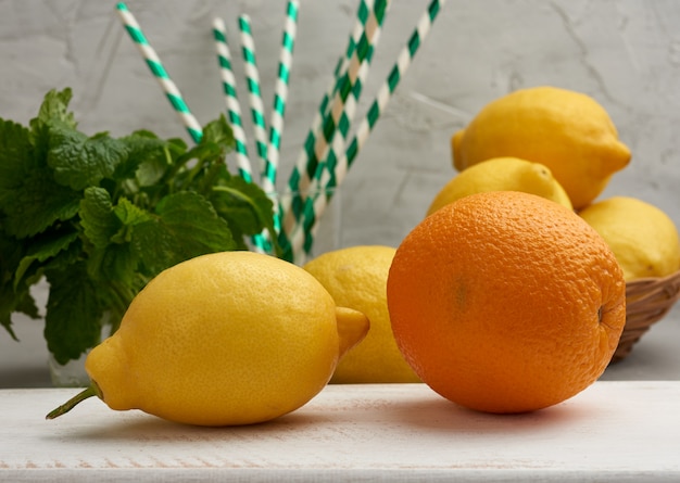 Intero arancio, giallo limone maturo e un mazzo di menta su un legno