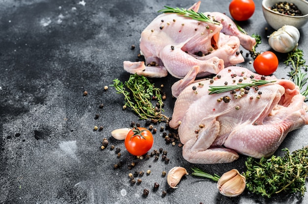 Intero pollo crudo dell'azienda agricola biologica con le erbe sul nero. Vista dall'alto. Copia spazio