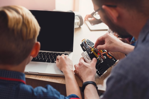 Invenzioni e creatività per i bambini. Robot di programmazione ragazzo irriconoscibile su laptop con insegnante. Educazione allo stelo. Sviluppo precoce, fai da te, innovazione, istruzione integrata, concetto di tecnologia moderna