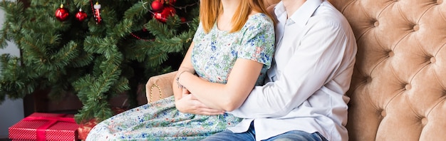 Inverno, amore, coppia, natale e concetto di persone - primo piano di un uomo e di una donna che si abbracciano sullo sfondo dell'albero di natale