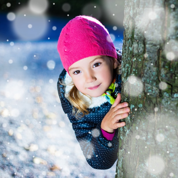 Inverno - bambina carina che si nasconde dietro un albero nel parco