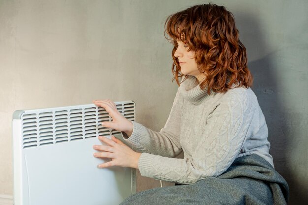 inverno freddo nell'appartamento una ragazza si scalda le mani vicino all'energia della stagione di riscaldamento della batteria del riscaldatore