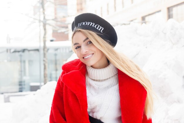 Inverno, moda, concetto di persone - moda Ritratto di una giovane e bella donna cammina per la città sorridente pelliccia rossa close-up fiocchi di neve freddo inverno, respirare aria fresca al giorno d'inverno gelo. tramonto