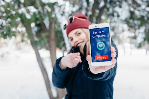 Inverno, natale, tecnologie, persone, stile di vita e concetto di bellezza: messaggio completato con pagamento sullo schermo di un telefono cellulare. Donna che mostra il suo telefono cellulare. Inverno donna che soffia neve in un parco.