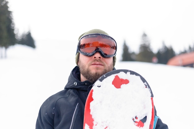 Inverno, tempo libero, sport e concetto di persone - Uomo che fa snowboard in montagna. Snowboarder che riposa sulla cima della montagna su uno sfondo di cielo blu. Stazione sciistica.