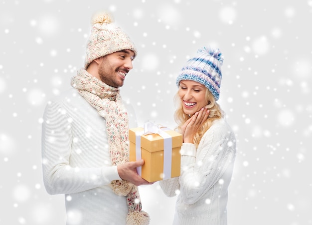 inverno, vacanze, coppia, natale e concetto di persone - uomo e donna sorridente in cappelli e sciarpa con confezione regalo