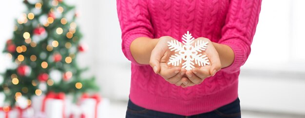 inverno, vacanze e concetto di persone - primo piano di donna in maglione rosa che tiene la decorazione del fiocco di neve sul soggiorno con lo sfondo delle luci dell'albero di natale